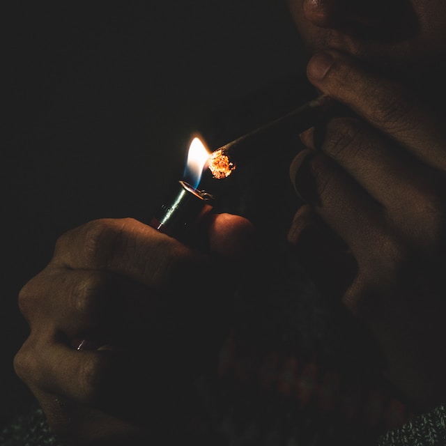 person in a dark room lighting a marijuana joint